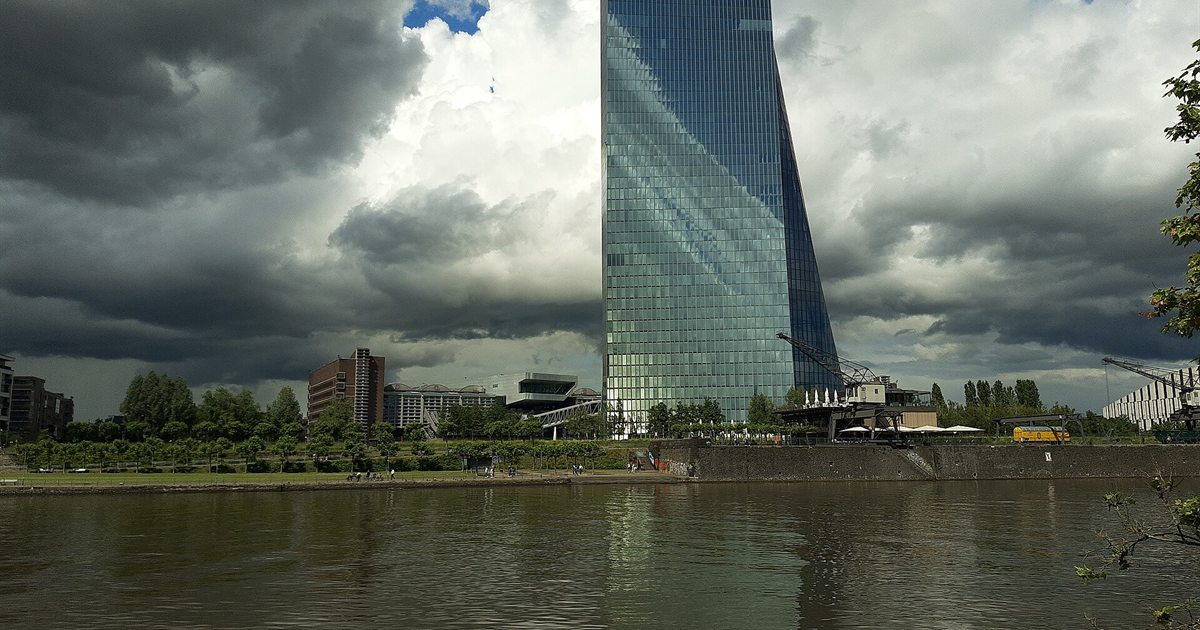 Storm clouds gathering over a glass tower beside a river