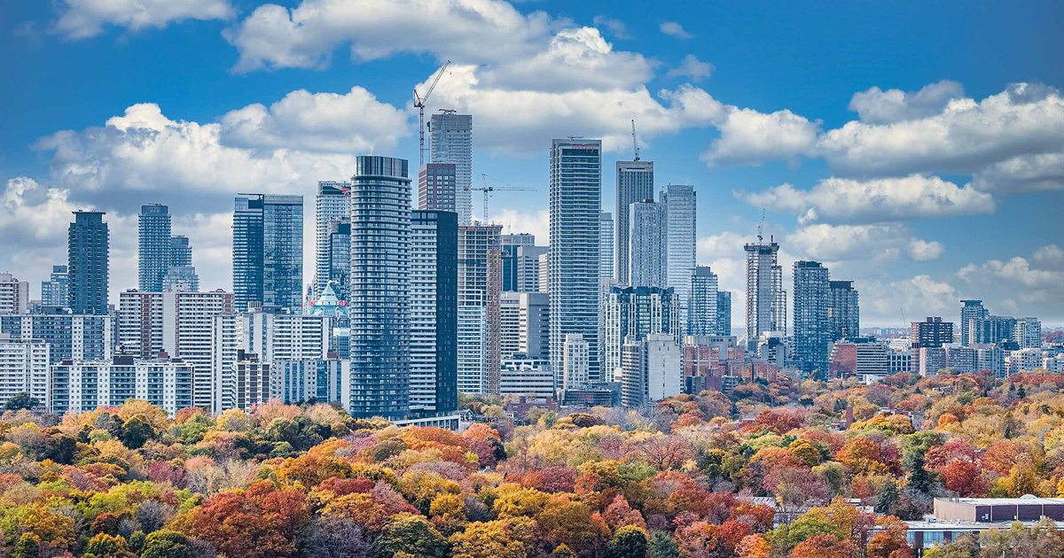 The Toronto skyline rising above a ravine of trees in bright autumn colours under a blue sky with scattered clouds