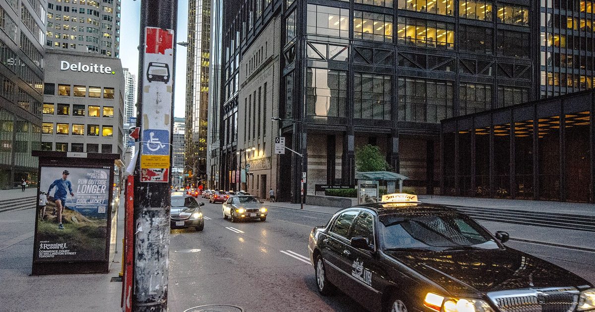 Bay Street in Toronto's financial district at dusk, with office towers on both sides and traffic in the road