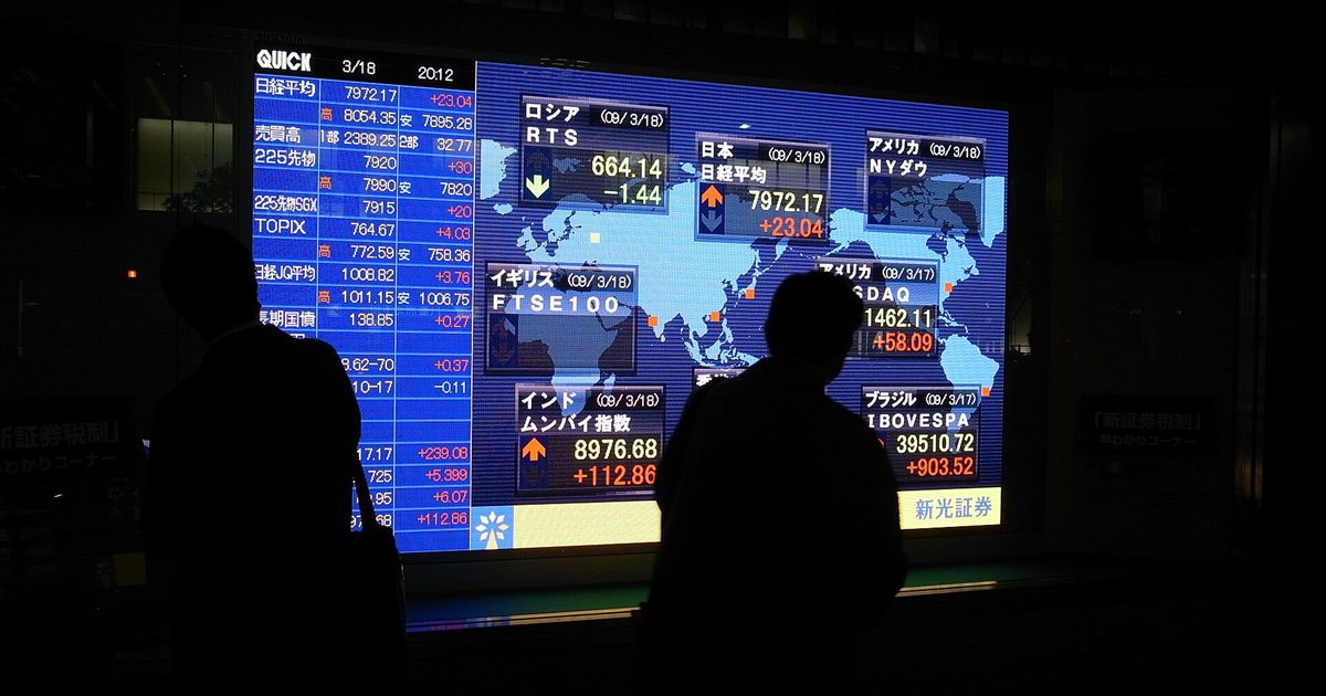 Silhouettes of people in front of an electronic world stock index board near Tokyo Station