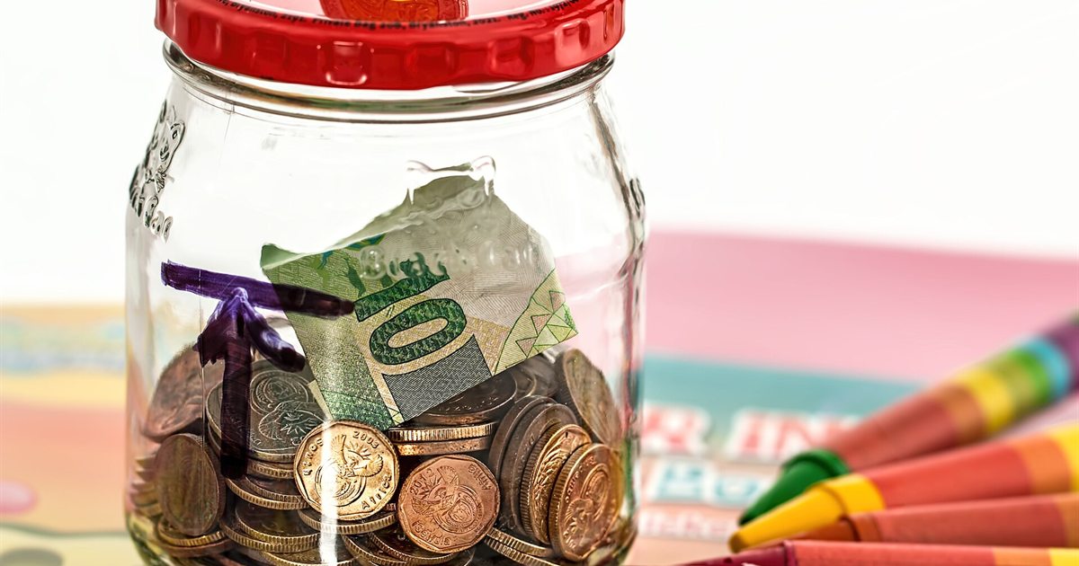 Coins and a folded banknote inside a glass savings jar on a white table