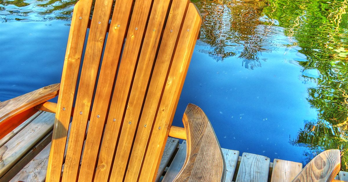 A wooden Muskoka chair on a dock overlooking a blue lake