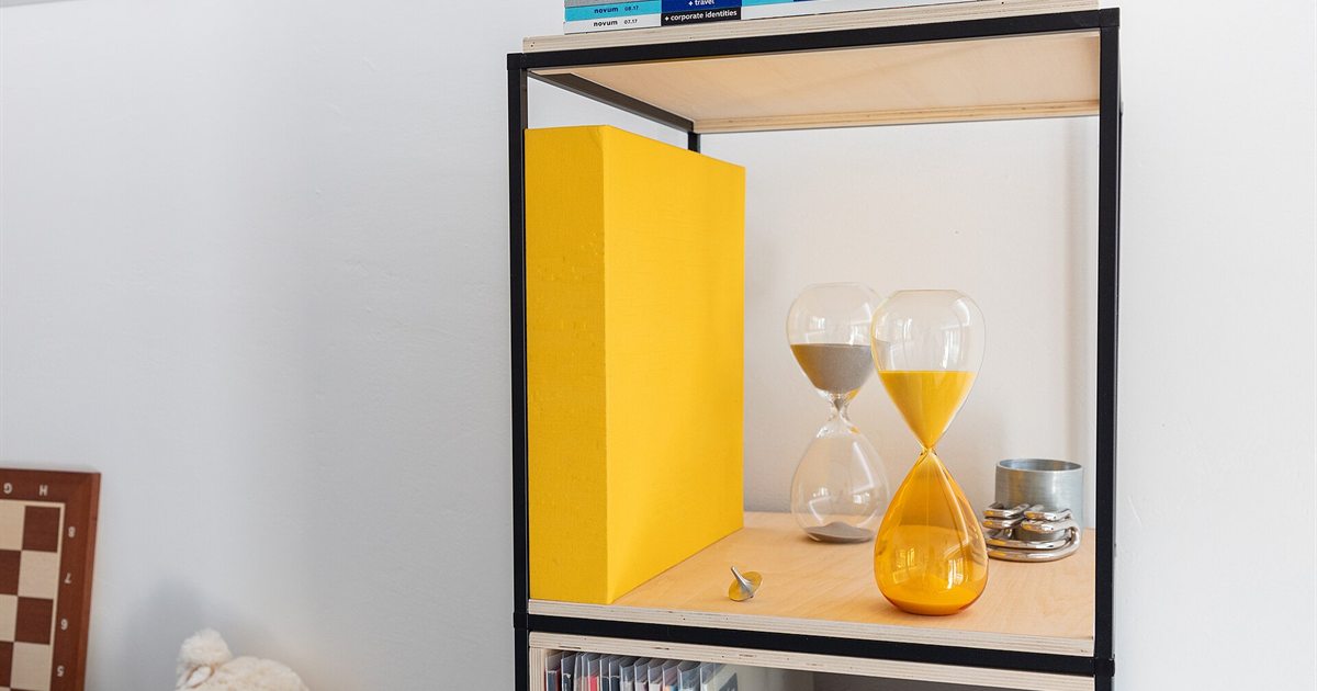 Two hourglasses with orange sand on a shelf beside a yellow box