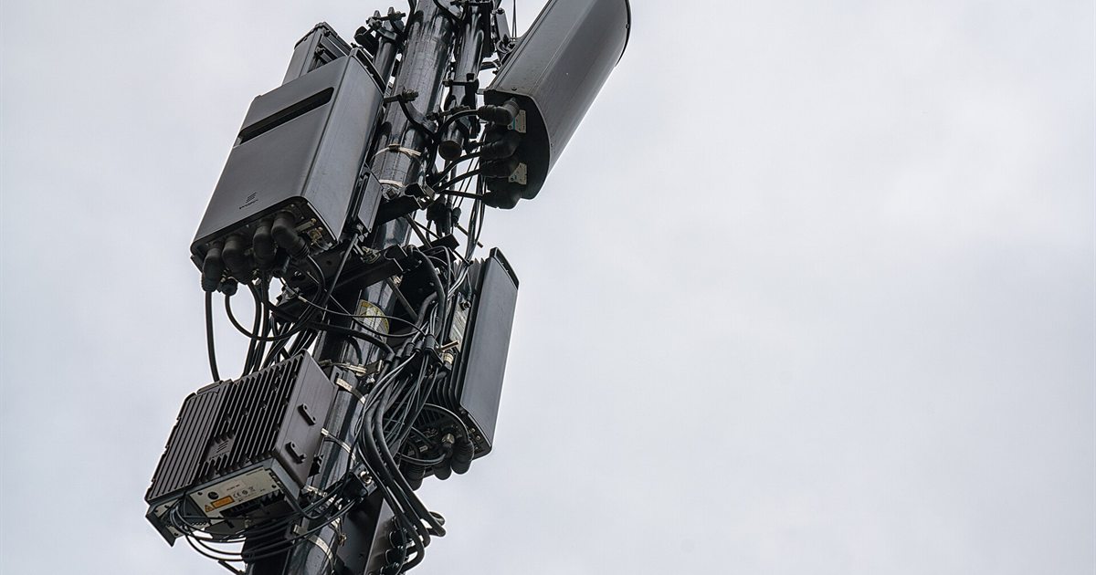 5G antennas and radio equipment mounted on a cellular tower against a grey sky