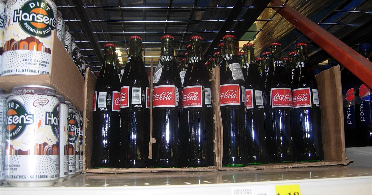 Glass bottles of Coca-Cola lined up on a store shelf