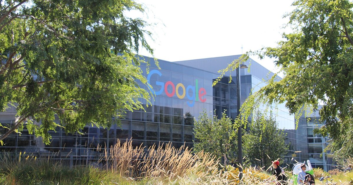 The glass Google headquarters building at the Googleplex in Mountain View, California, seen through trees