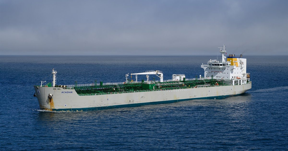 A large oil tanker with a white hull and green deck sailing across open blue water under a grey sky