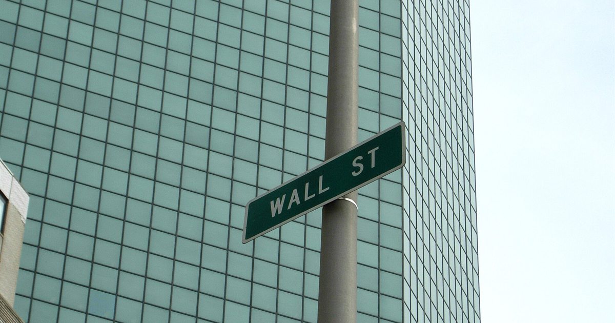 A green Wall St street sign in front of a glass office tower in New York's Financial District