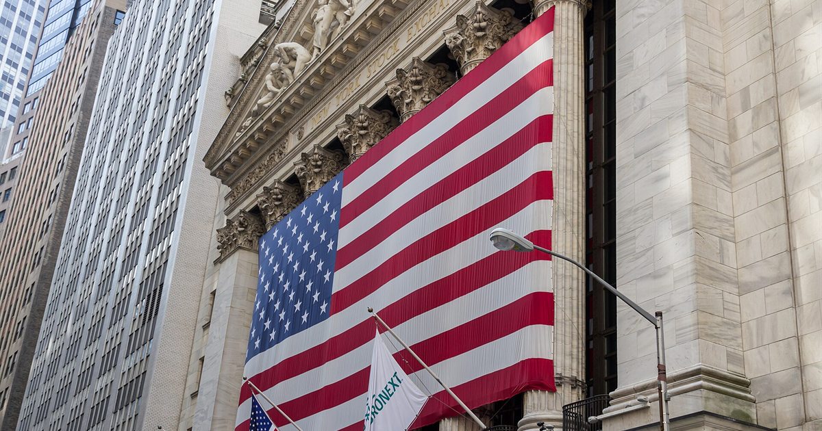 The New York Stock Exchange building on Wall Street with a large American flag hanging across its columns