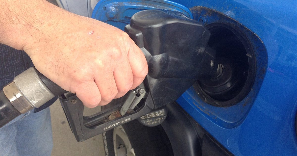 A hand holding a gasoline pump nozzle while filling a car's fuel tank