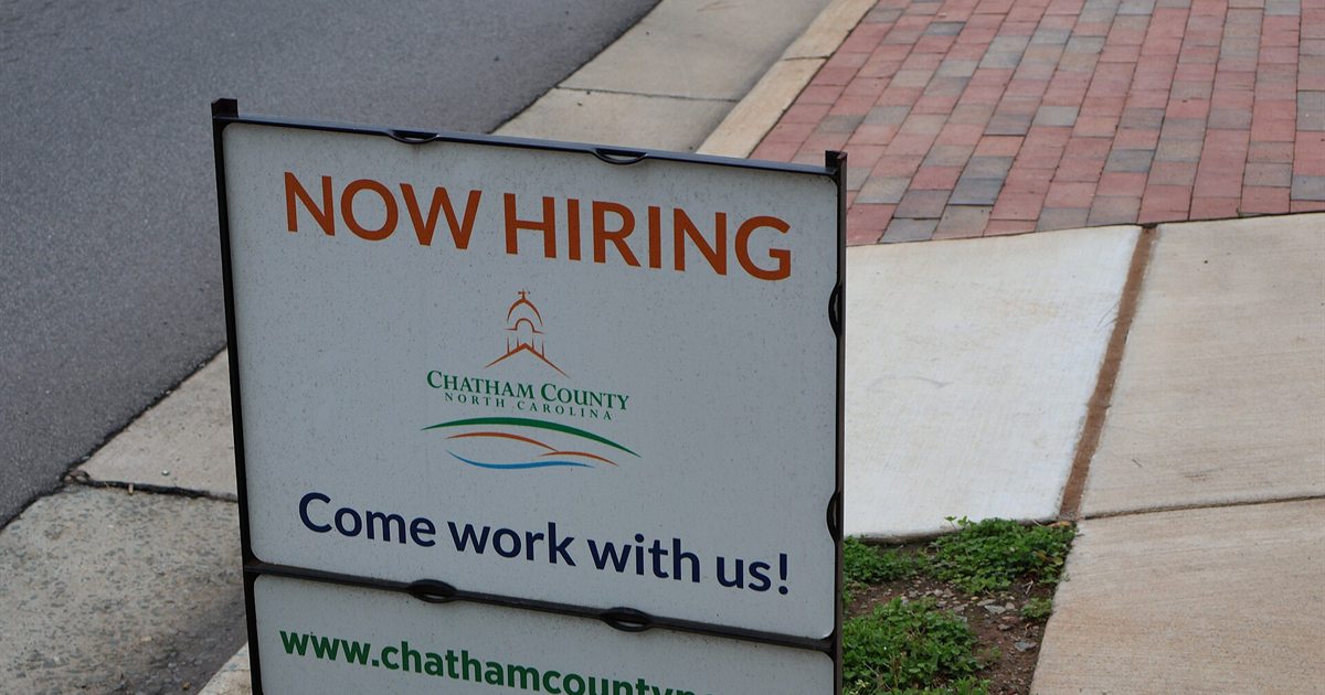 A roadside Now Hiring sign inviting people to apply for work